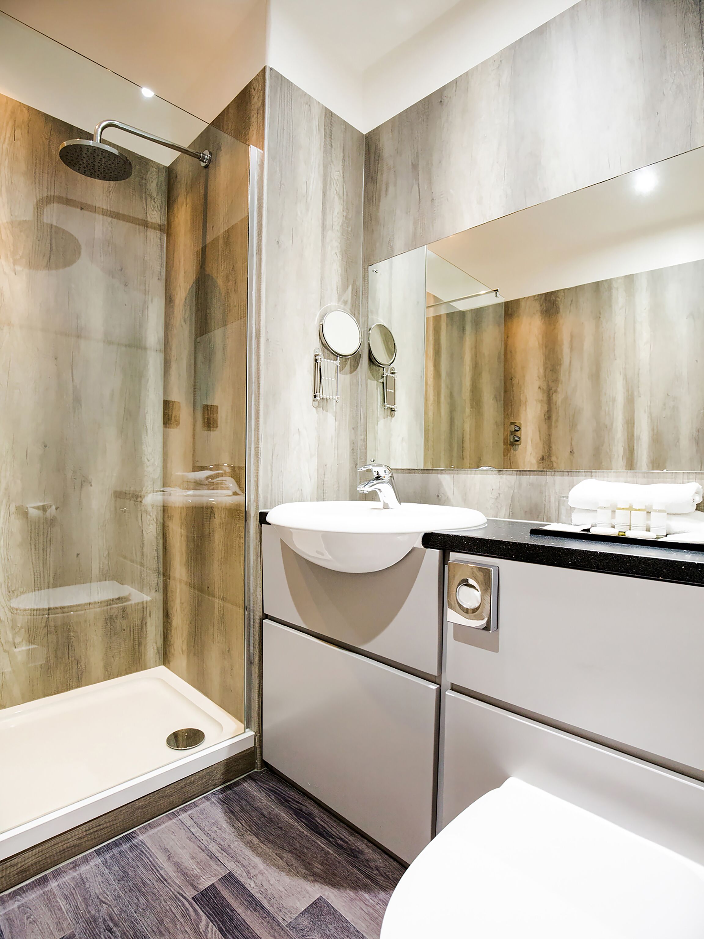 A modern bathroom with a glass shower enclosure, a sink with a vanity, and a large mirror.