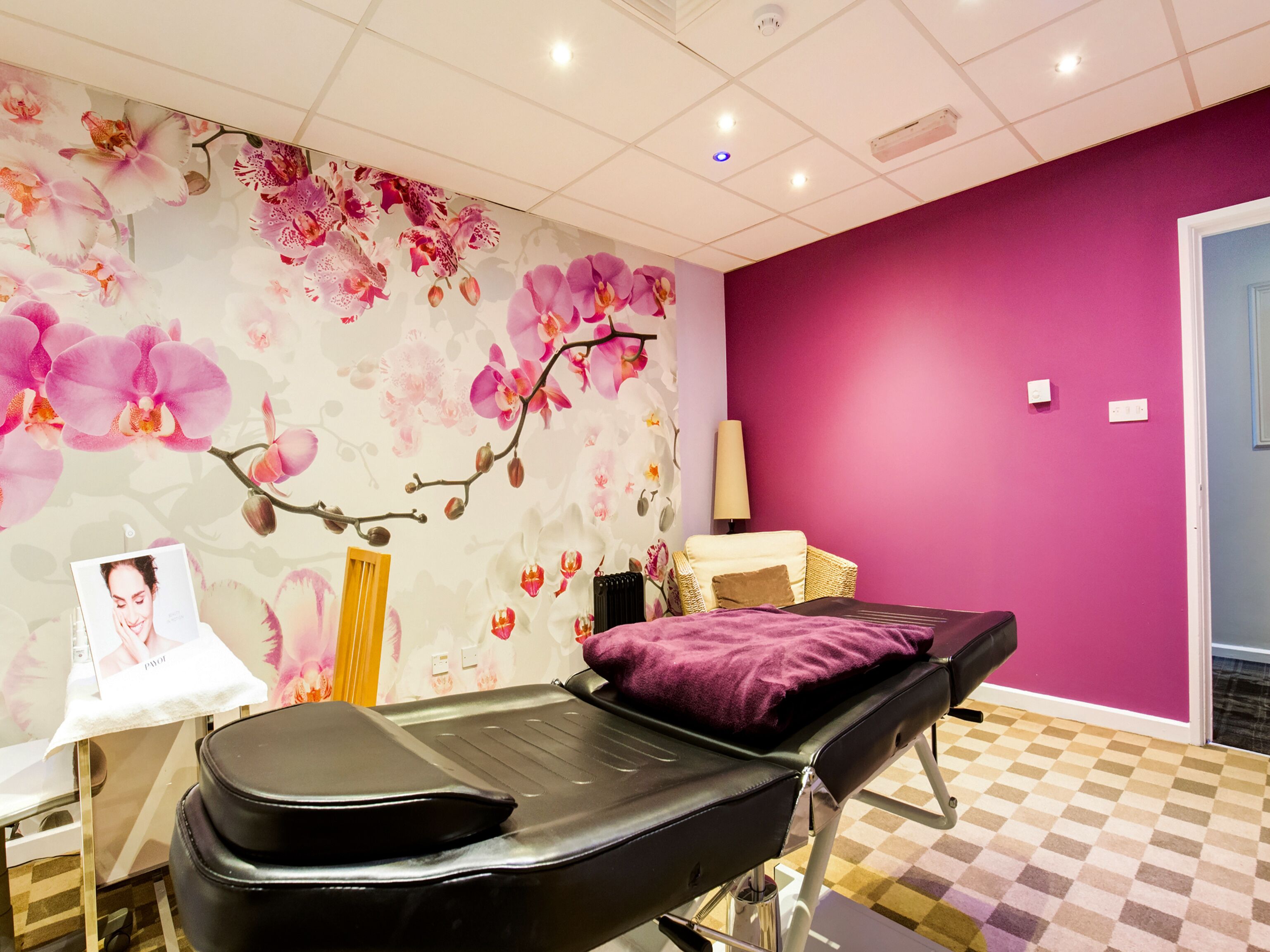 A room with a checkered floor, a purple wall, and a bed with a purple pillow.