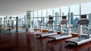 Ein Fitnessstudio mit Laufbändern, Kraftgeräten und Blick auf die Stadt durch große Fenster.