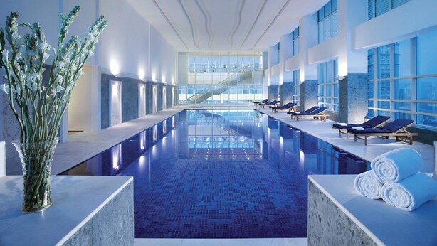 Ein moderner, überdachter Swimmingpool mit Panoramafenstern, Liegestühlen und Blick auf die Stadt.