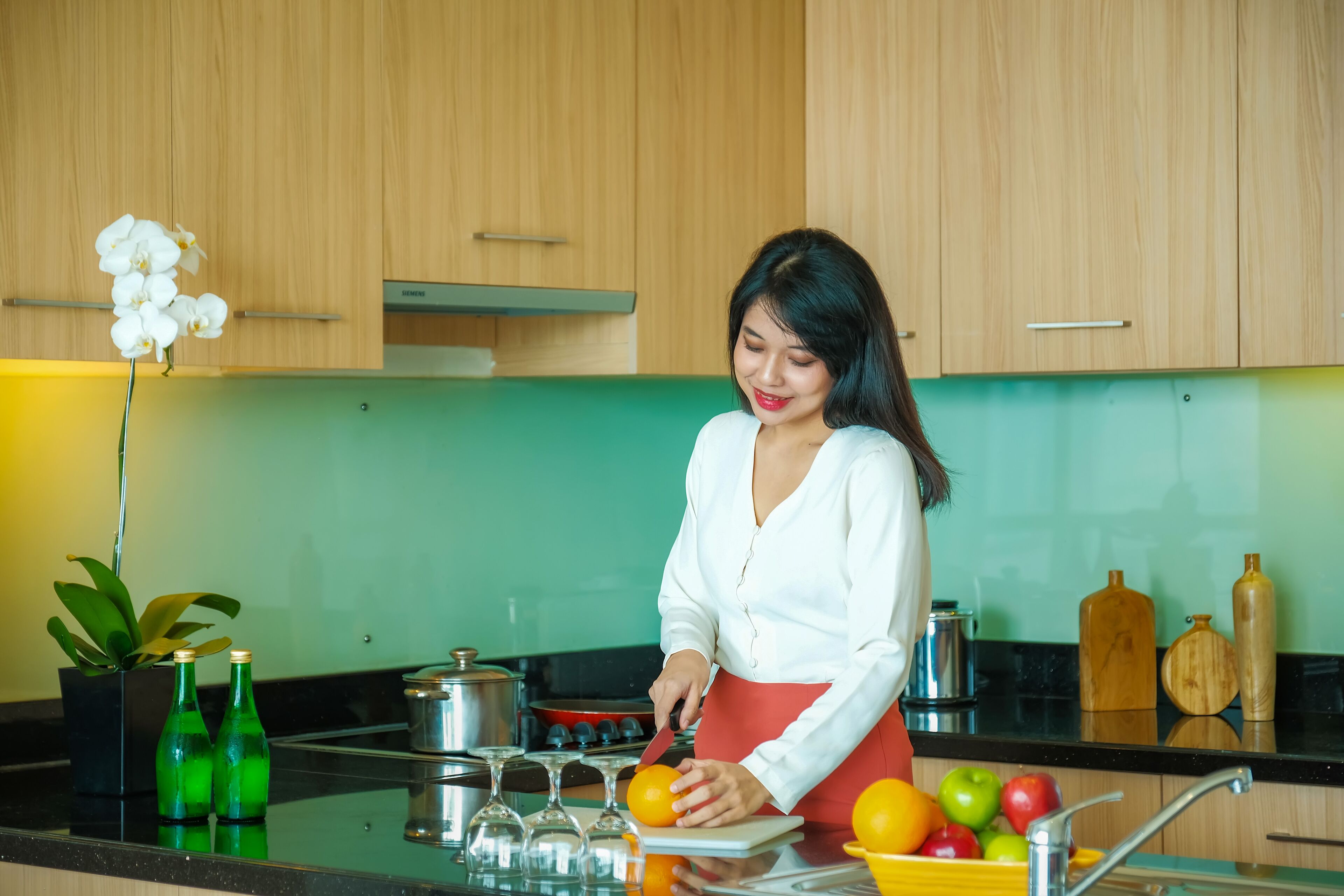 A kitchen with wooden cabinets, a green backsplash, and a person preparing fruit.