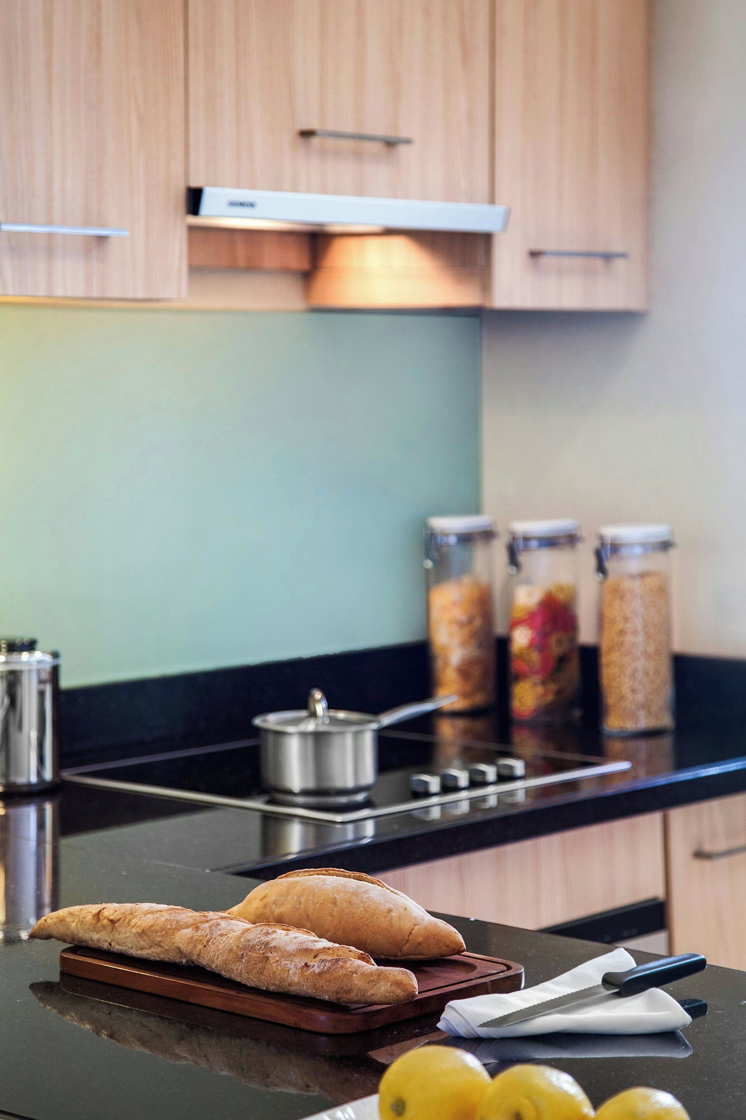 Un plan de travail de cuisine avec deux pains, une planche à découper, un couteau et trois bocaux en verre contenant divers aliments.