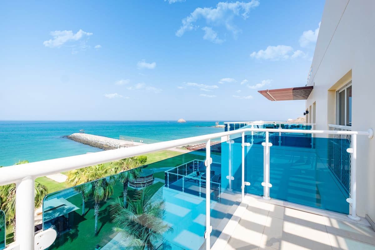 A balcony with a glass railing overlooking a pool and ocean.