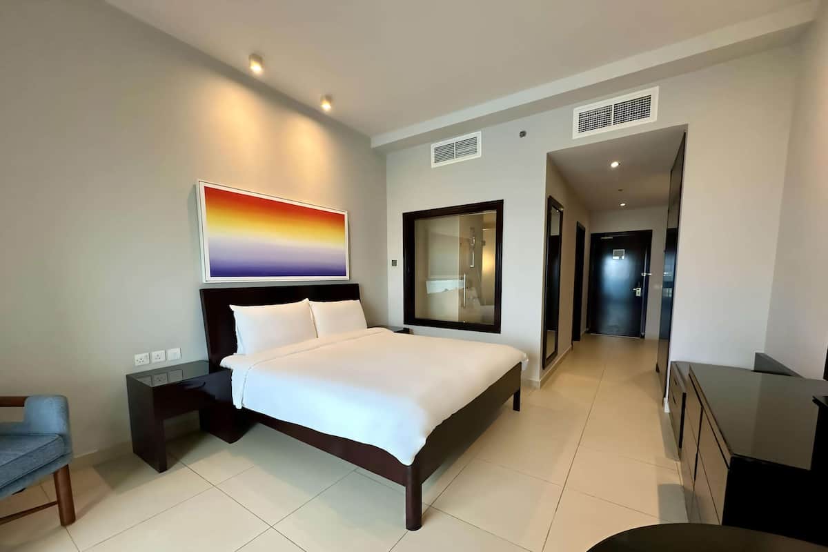 A modern hotel room with a large bed, a desk, a chair, and a painting on the wall.