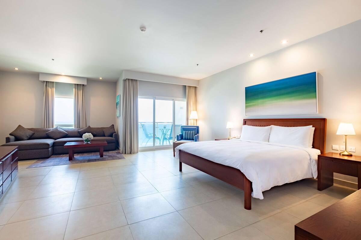 A hotel room with a bed, a sofa, a coffee table, a desk, and a balcony with a view.