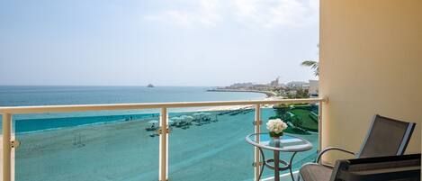 A balcony with a view of a beach and ocean, a small table with a vase, and two chairs.