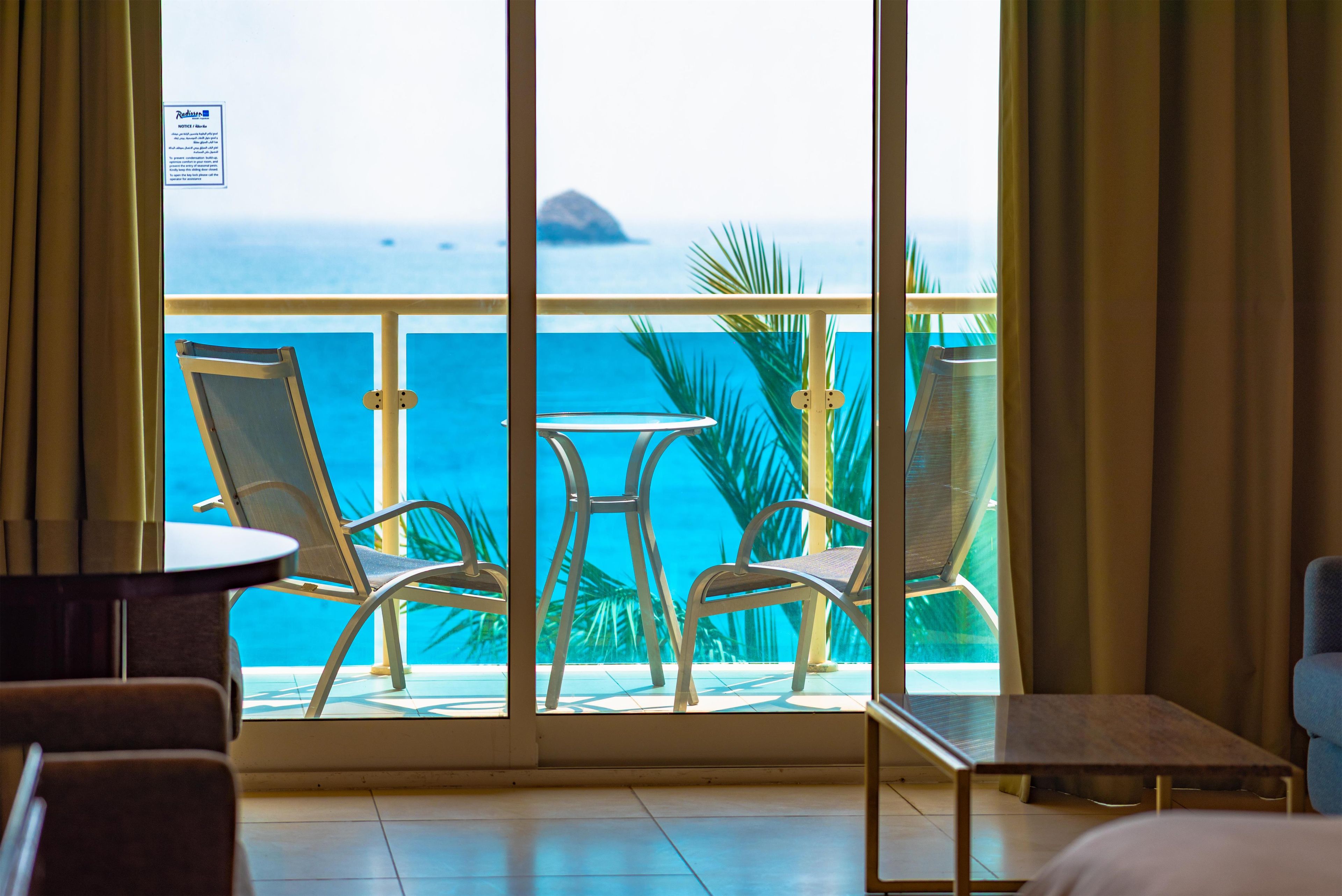 A balcony with two chairs and a small table, overlooking a pool and a view of the ocean.