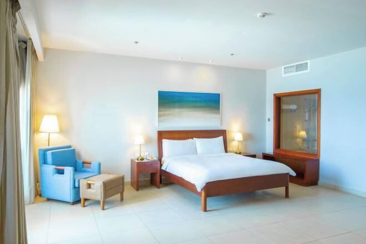 A hotel room with a bed, a chair, a nightstand, a lamp, and a painting on the wall.