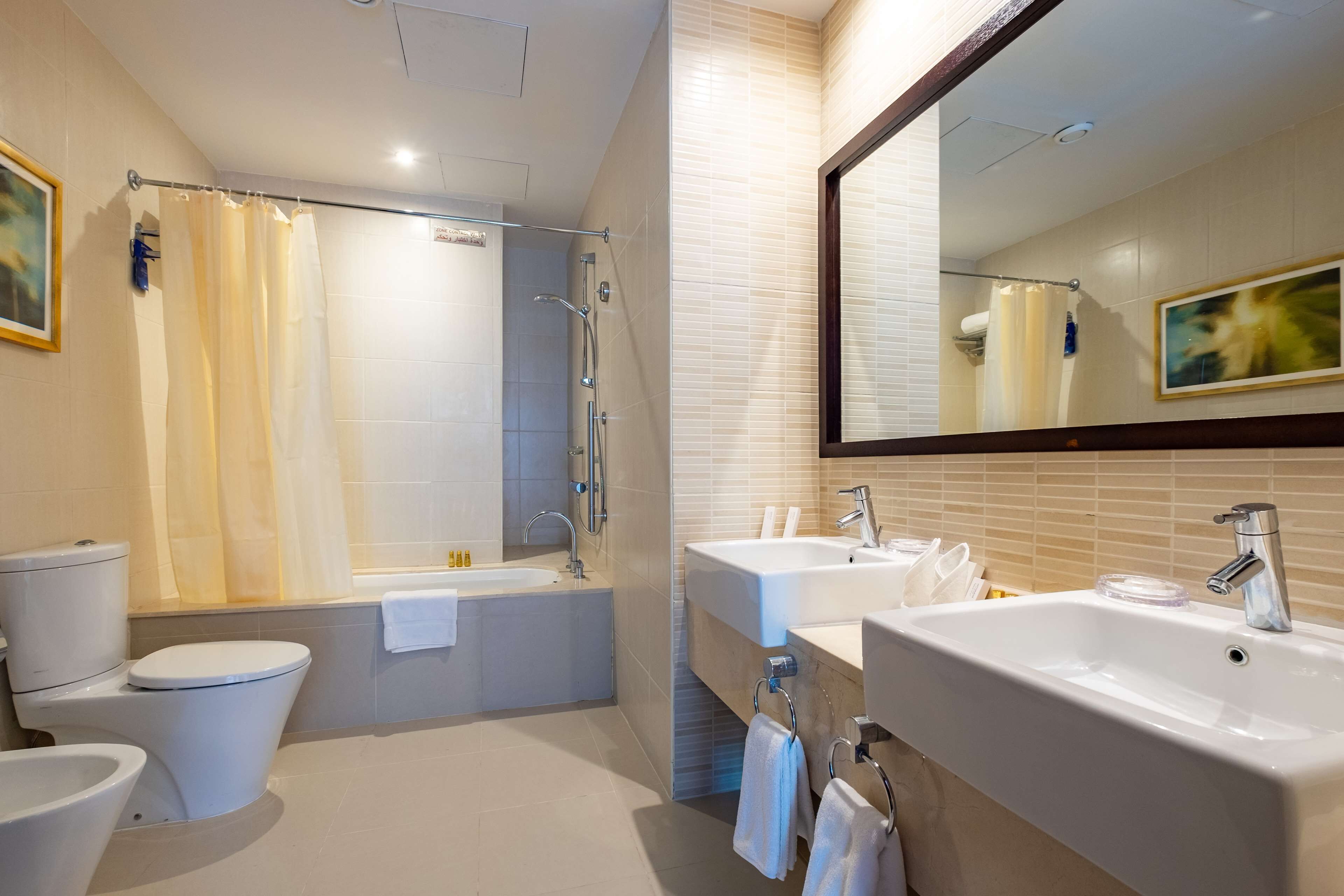 A modern bathroom with a toilet, bidet, bathtub, and two sinks.