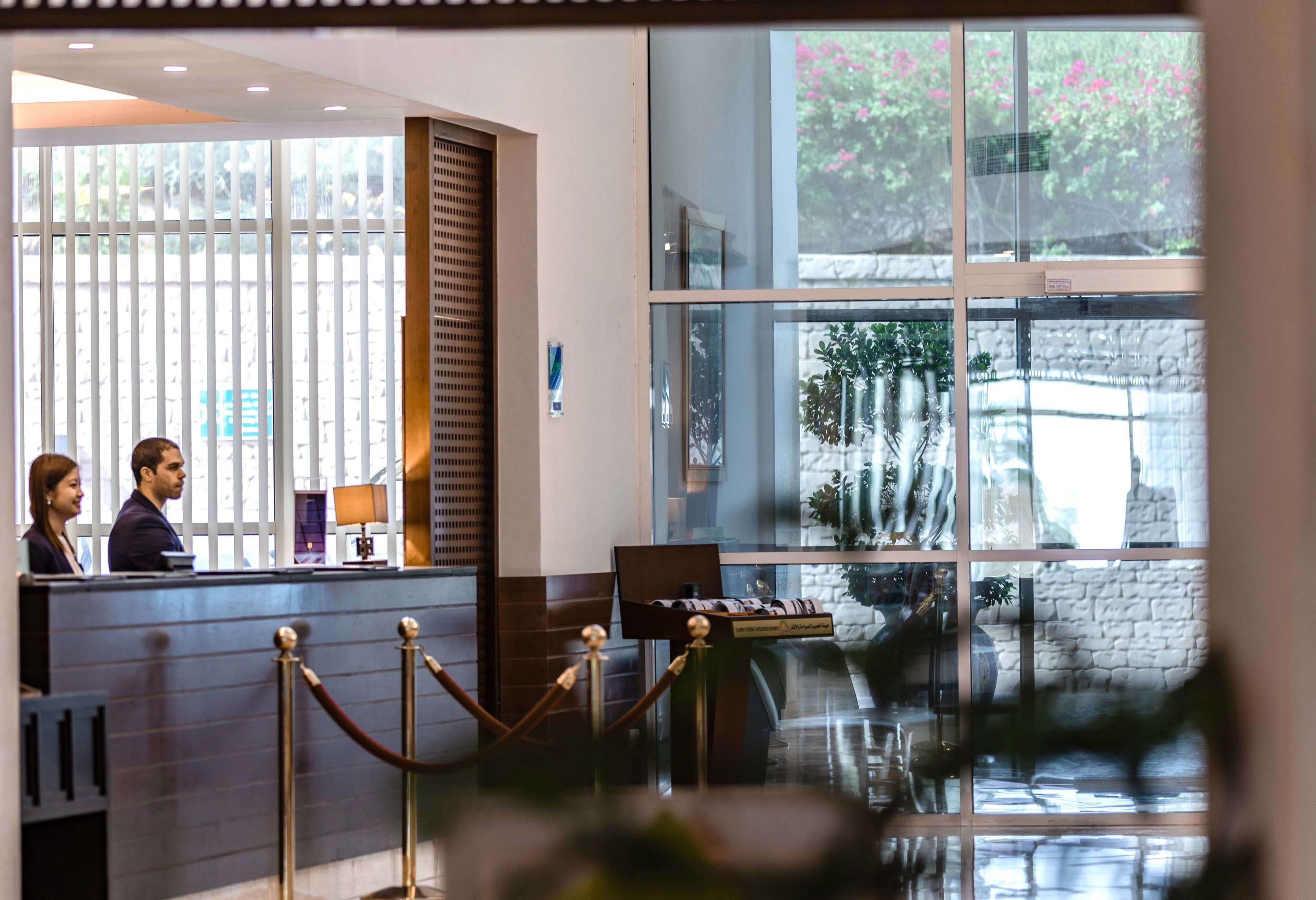 A reception area with a counter, a glass partition, and a view of a garden through large windows.