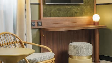 A hotel room with a wooden vanity, a flat-screen TV, a round table with wicker chairs, and a patterned rug.