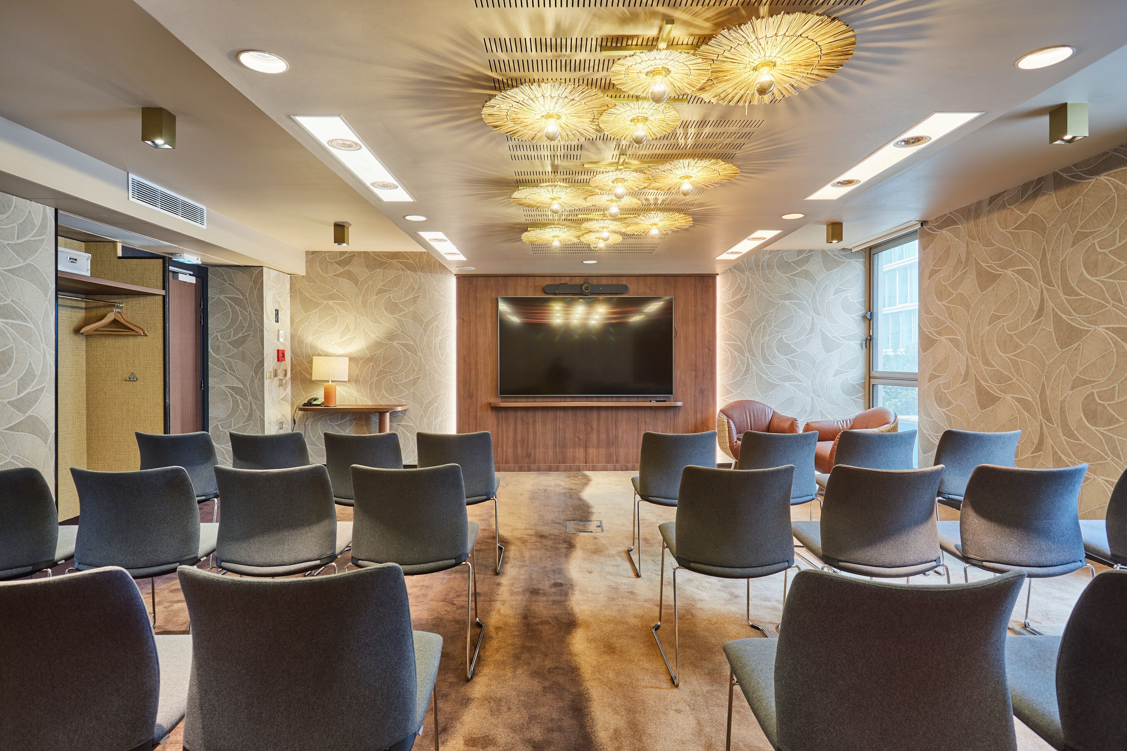 A conference room with a large flat-screen TV, rows of chairs, and a patterned carpet.