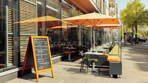 An outdoor cafe with tables and chairs, a chalkboard menu, and orange umbrellas. - voco Paris – Porte de Clichy by IHG (Clichy)