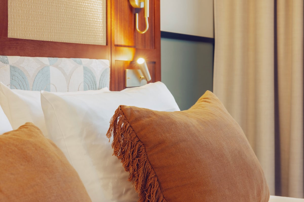 A hotel room with a bed featuring white and brown pillows, a wooden headboard, and a wall-mounted telephone.