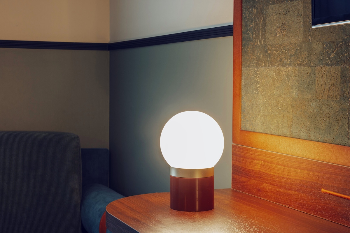 A modern room with a wooden sideboard, a round table lamp, and a blue upholstered chair.