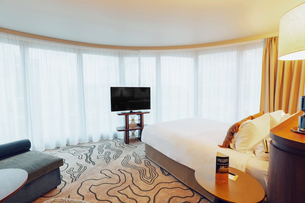 A hotel room with a large bed, a sofa, a TV on a stand, and a patterned carpet.