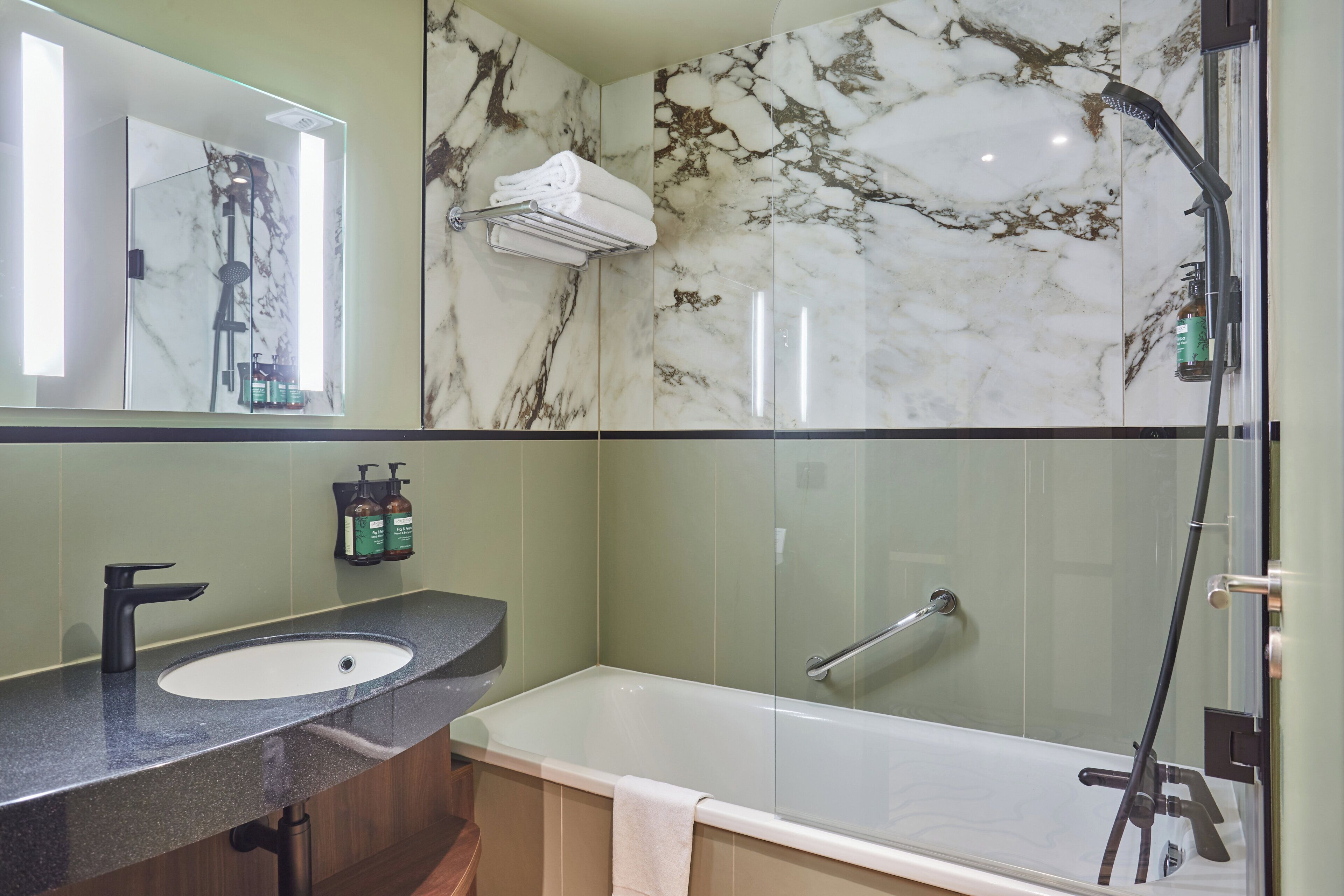 Un baño moderno con salpicadero de mármol, una bañera independiente, un tocador con lavabo y un espejo.