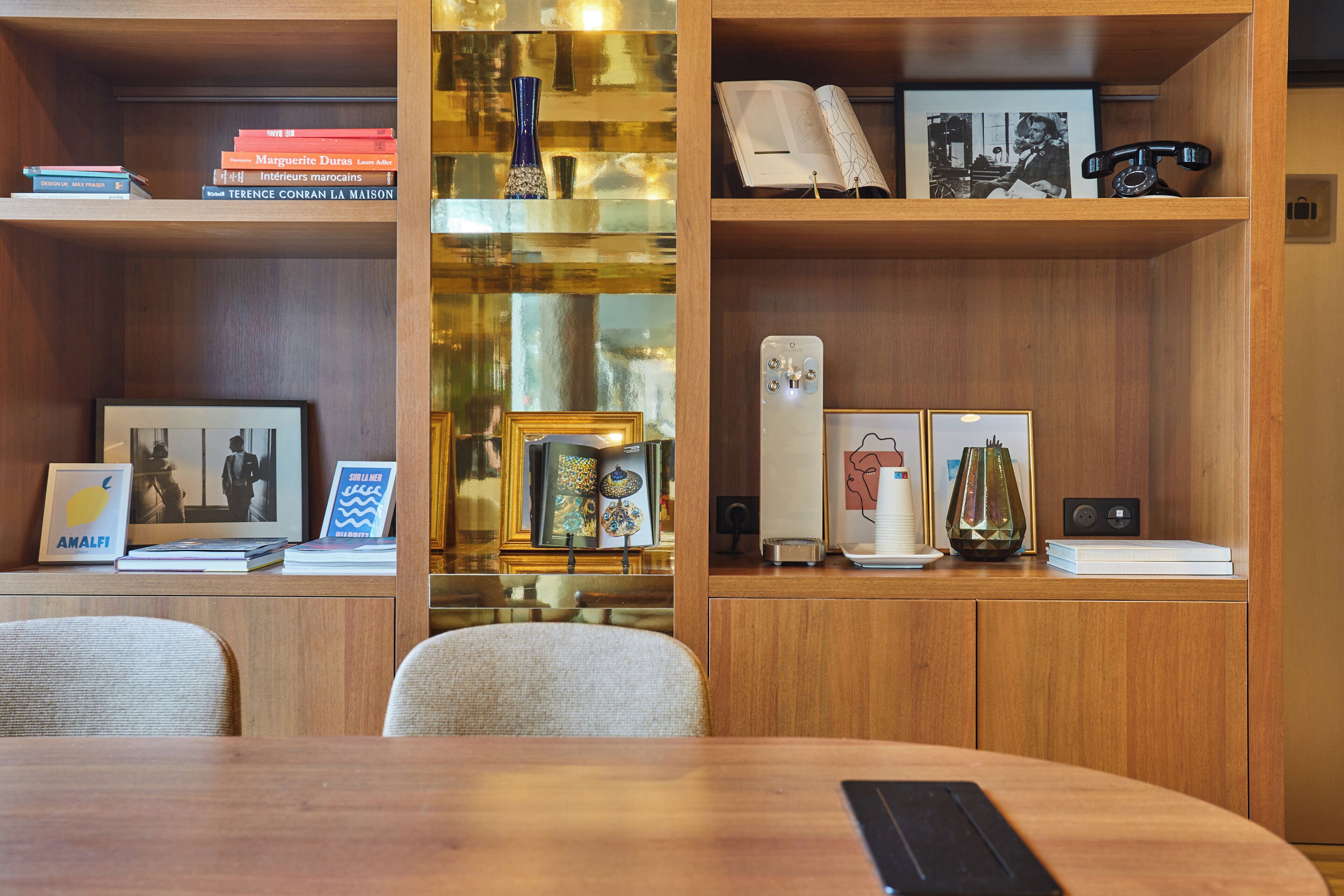 Een moderne, overzichtelijke kamer met houten planken vol boeken, ingelijste foto’s en decoratieve objecten.