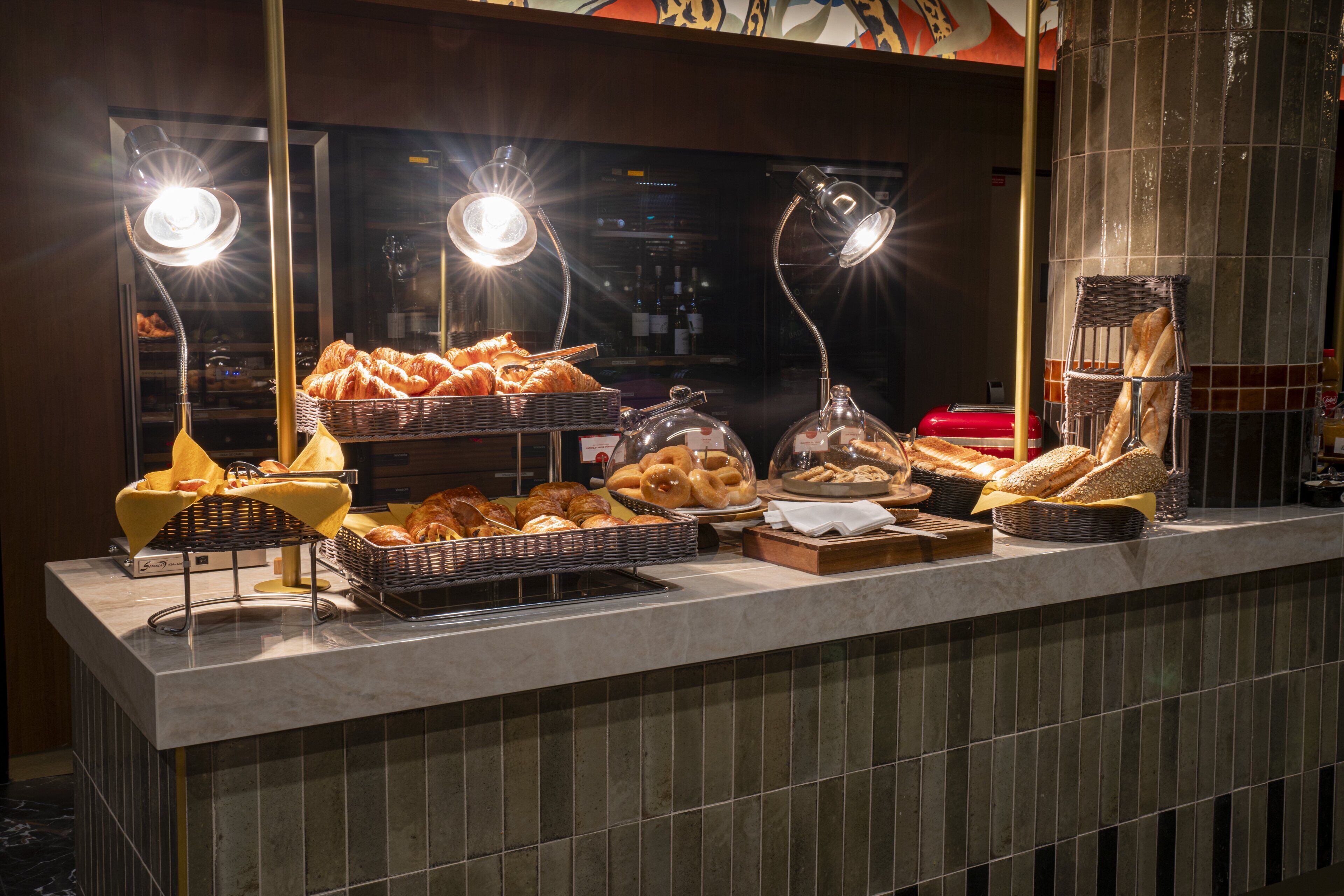 Un bufé de desayuno con panes y bollería de diferentes tipos, presentados bajo luces brillantes.
