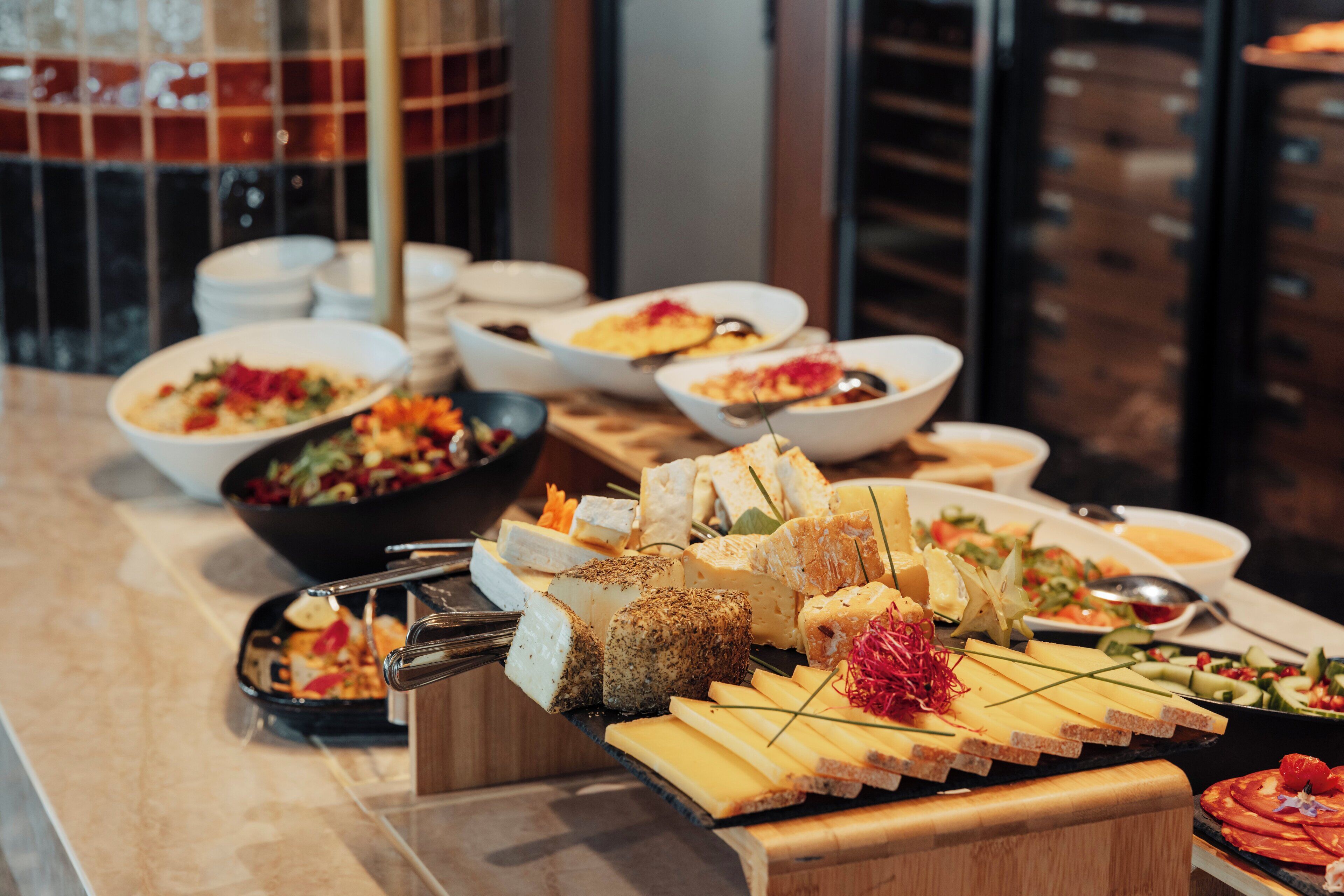 A buffet with various dishes including cheeses, meats, and salads.