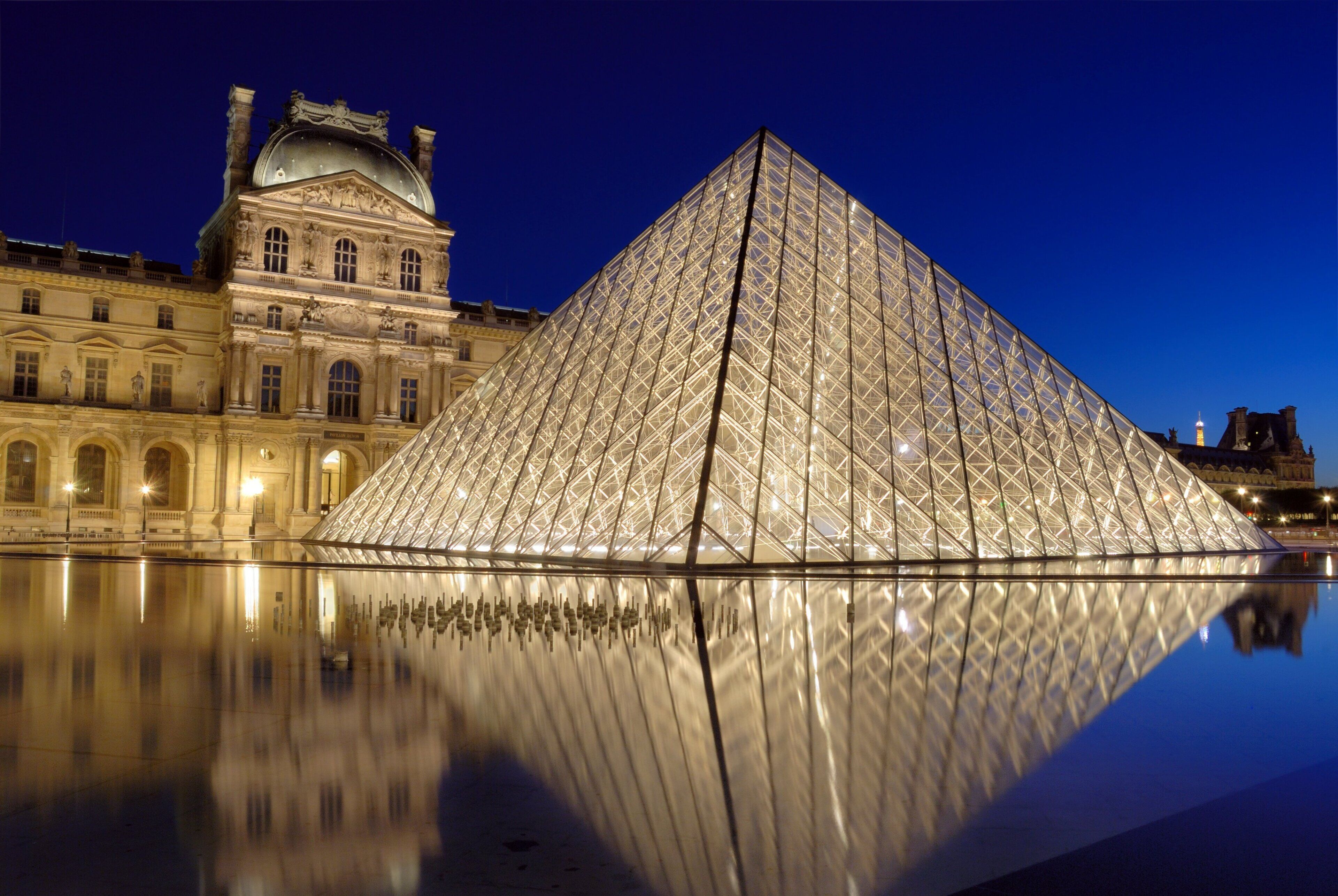 La pyramide du Louvre, avec son reflet dans l’eau, est entourée d’une architecture classique.