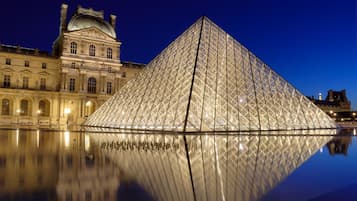 The Louvre Pyramid with its reflection in the water, surrounded by classical architecture.