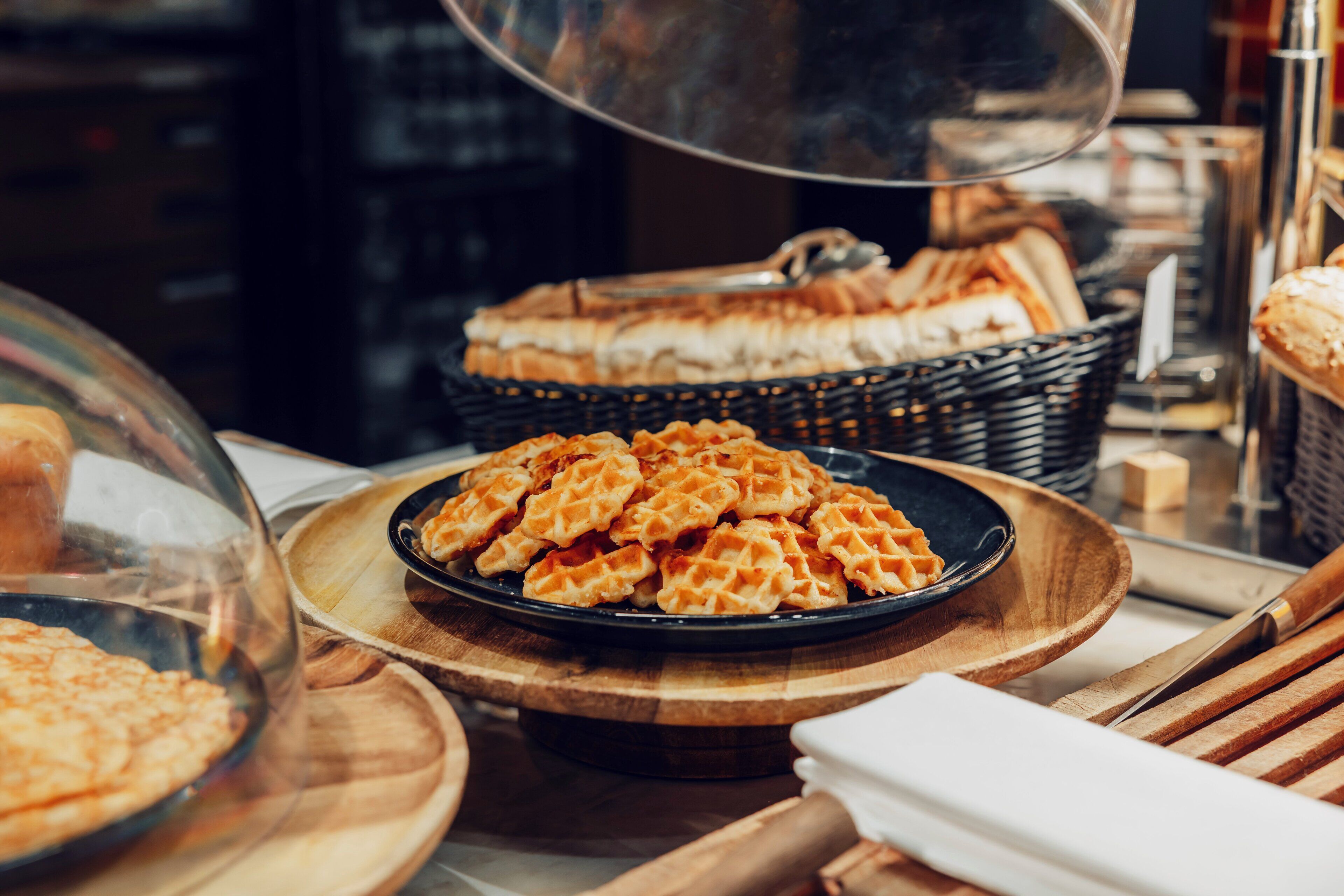 A display of waffles and pastries on wooden trays in a bakery setting.
