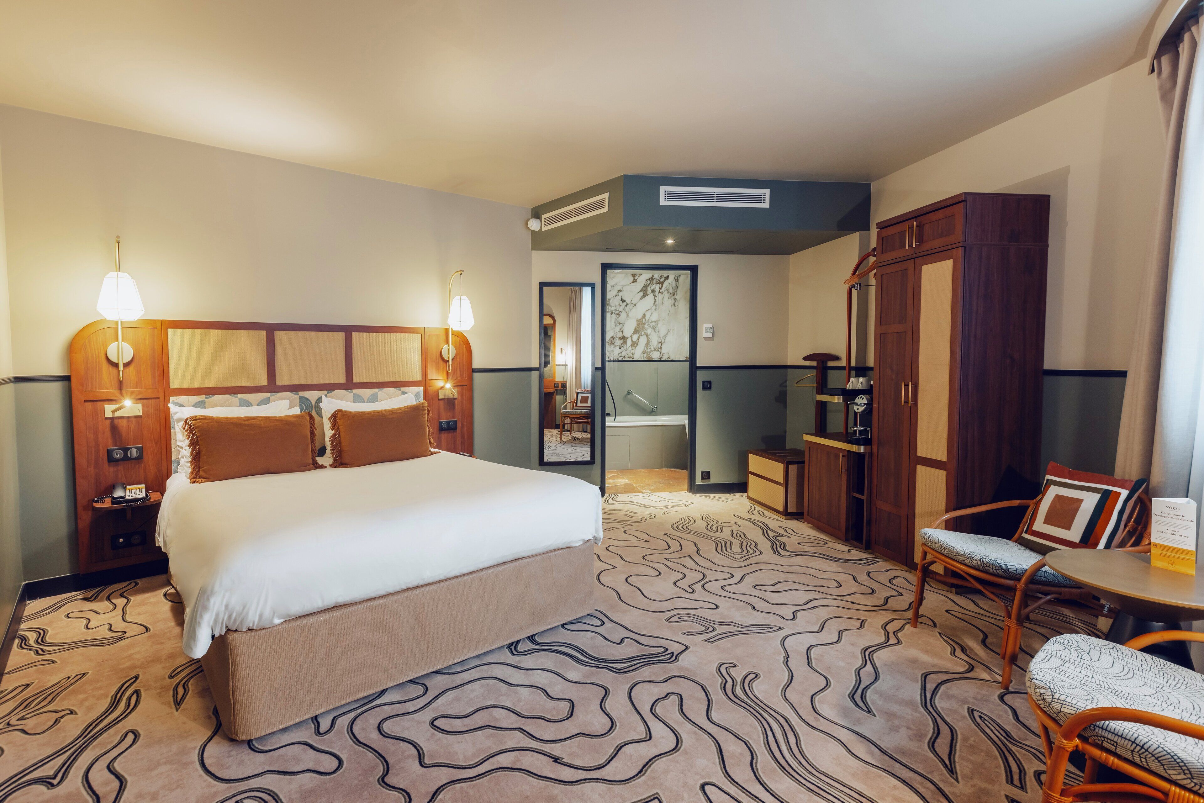 A hotel room with a large bed, bedside lamps, a wardrobe, a chair, and a small table.
