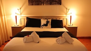 A hotel room with a bed, two bedside lamps, a cityscape view, and a pillow with a silhouette design. - Le Bay Lodge (Cape Town)