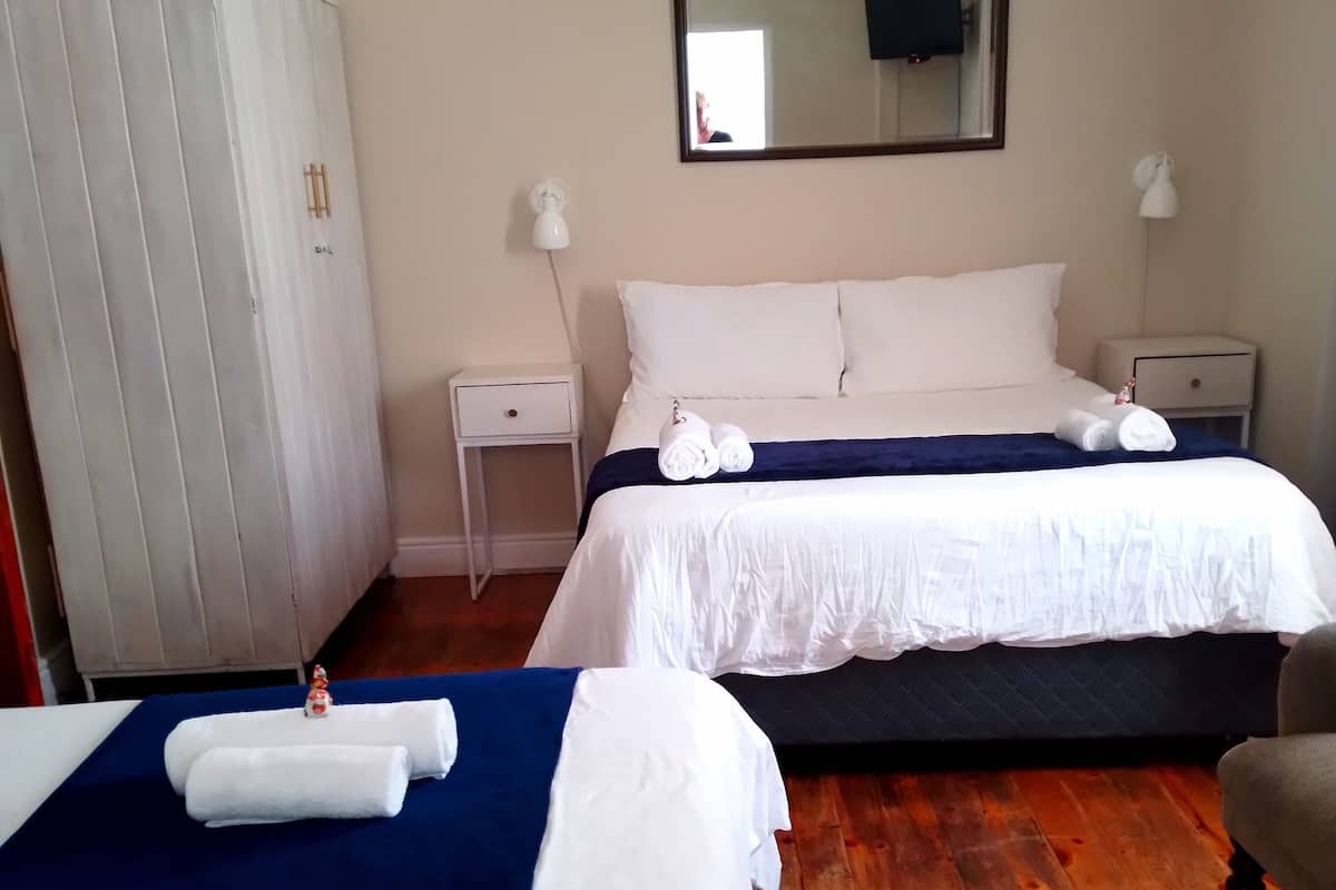 A hotel room with two beds, a wardrobe, a bedside table, a mirror, and a TV.