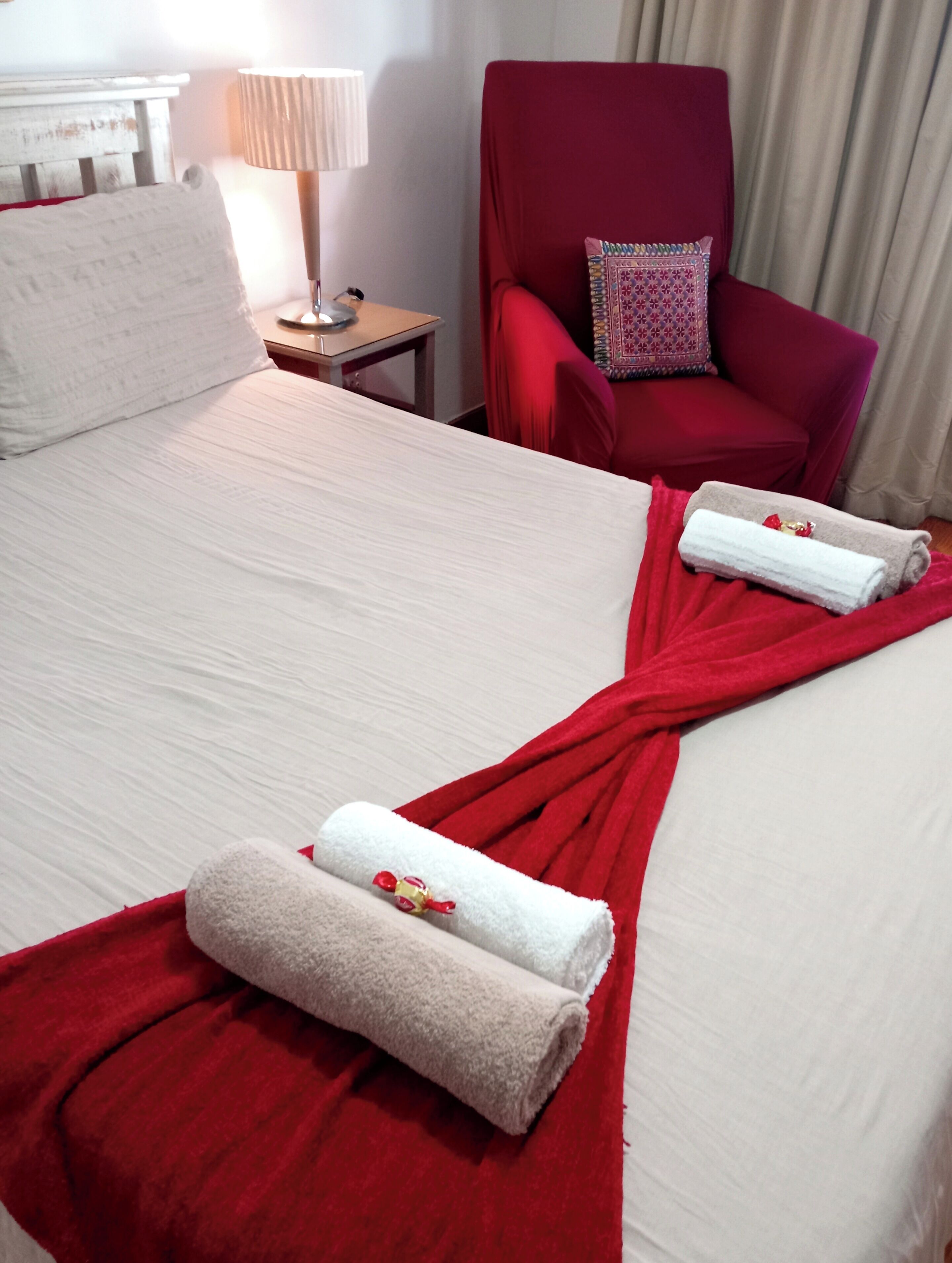 Una habitación de hotel con una cama grande, dos toallas rojas, un sillón rojo y una lámpara.
