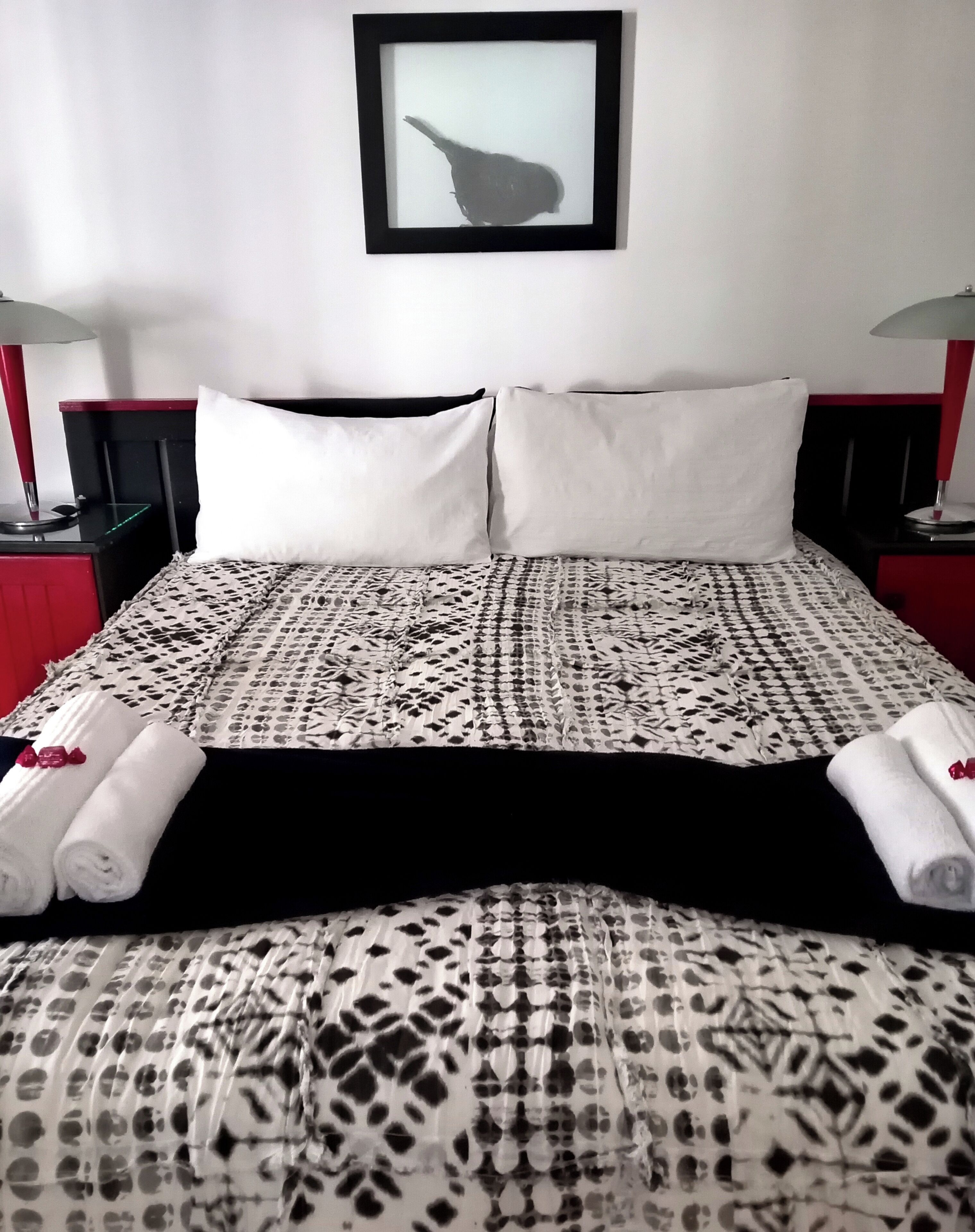 A neatly made bed with patterned bedding, two white pillows, and rolled towels on the side.