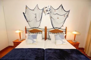 A double bed with a dark blue bedspread, two nightstands with lamps, and a wall-mounted decorative net. - Le Bay Lodge (Cape Town)