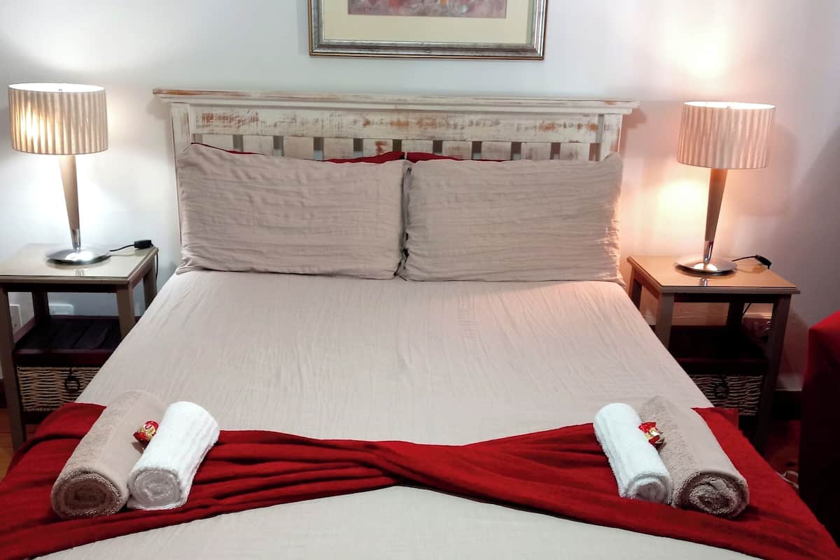 A neatly made bed with a red blanket and two rolled towels, two bedside lamps, and a framed artwork above the bed.