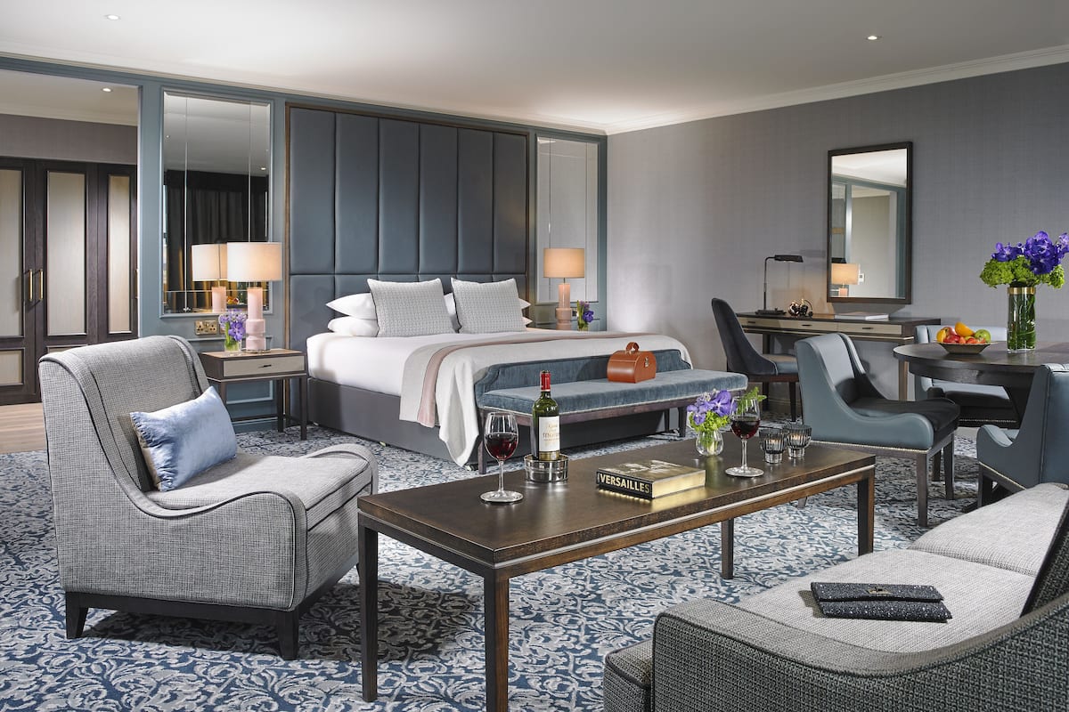 A modern hotel room with a large bed, a desk, and a seating area with chairs and a sofa.