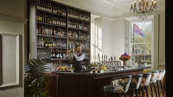 A bar area with a bartender, a large wine and liquor shelf, bar stools, and a chandelier.