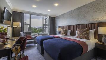 Una habitación de hotel con dos camas, un escritorio con silla, televisión y un ventanal con vista a la ciudad.