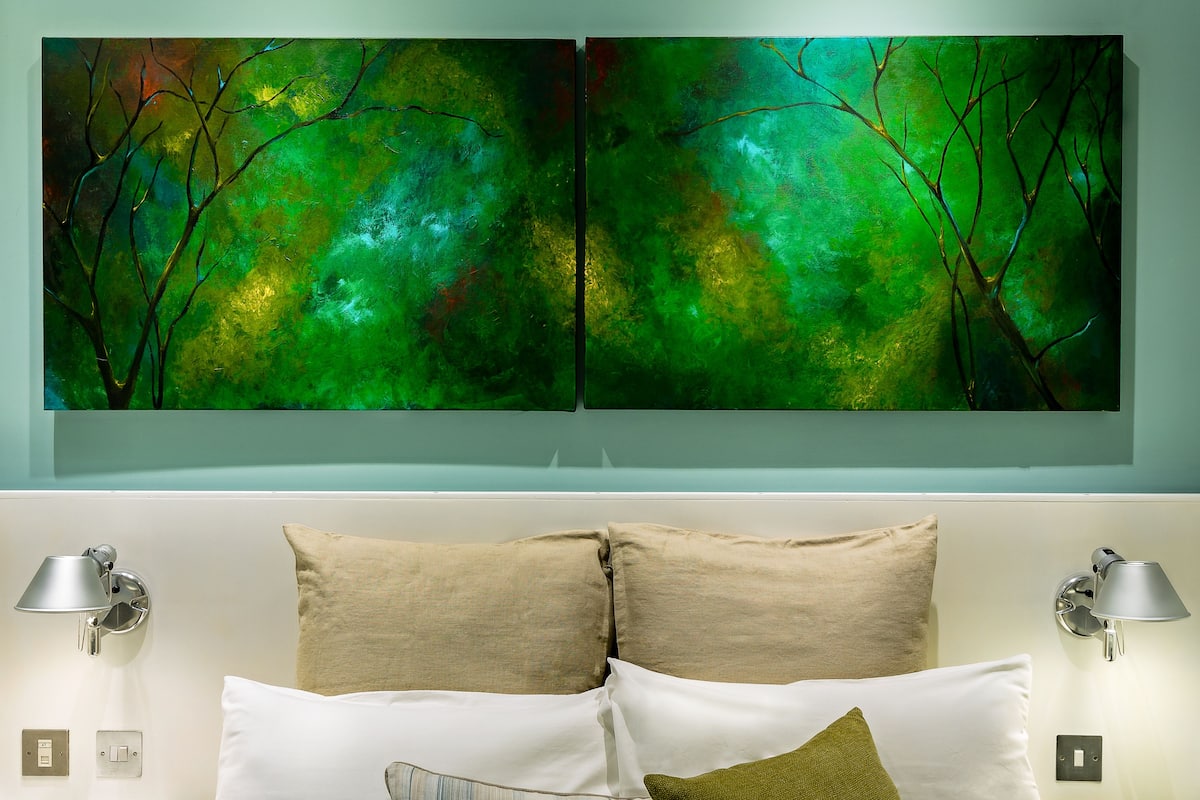 Une chambre avec un lit, deux lampes fixées au mur et deux tableaux au-dessus du lit.