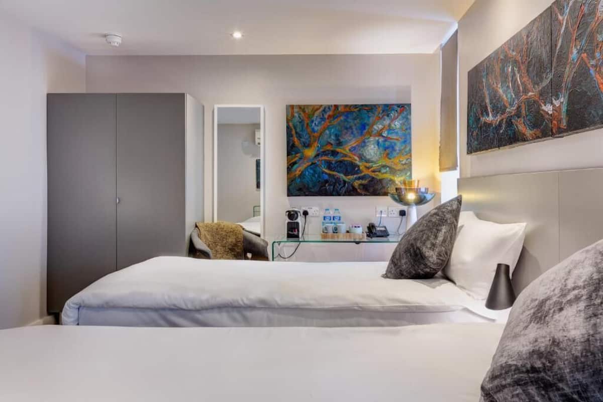 Une chambre d’hôtel moderne, dotée d’un grand lit, d’un bureau avec une lampe, d’une armoire et de tableaux abstraits accrochés aux murs.