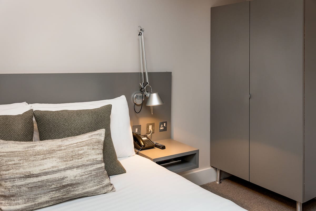 Une chambre d’hôtel comprenant un lit, une table de chevet avec une lampe, un téléphone et une armoire.