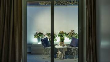 Una habitación con puerta de vidrio corrediza que da a un balcón exterior con dos sillas y plantas en macetas.