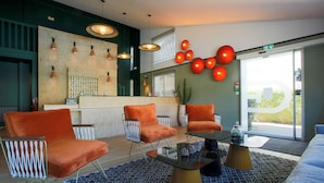 Un área de descanso moderna con sillones naranjas, una mesa de centro de cristal e iluminación colgante.