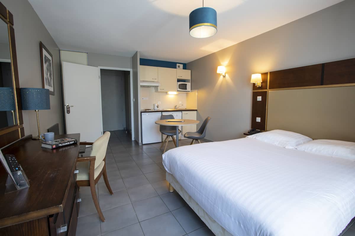Ein Hotelzimmer mit Bett, Schreibtisch mit Stuhl, einer kleinen Küchenzeile und einem Essbereich.