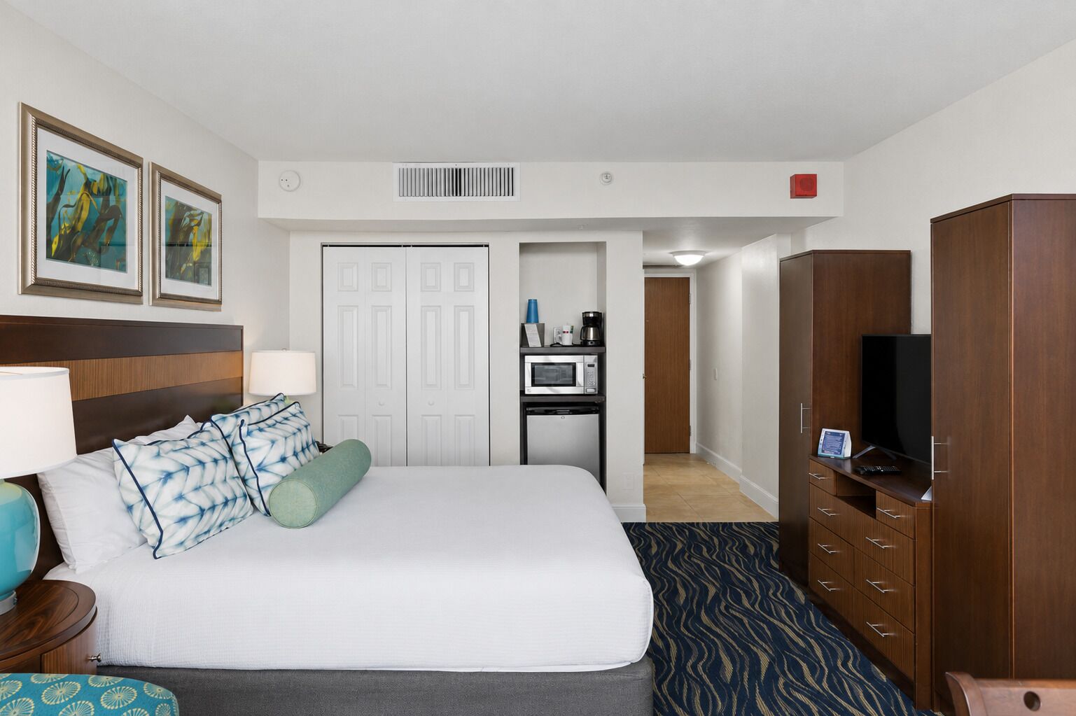 Habitación de hotel con cama, escritorio con microondas, televisor y armario.