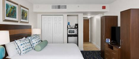 Habitación de hotel con cama, escritorio con microondas, televisor y armario.