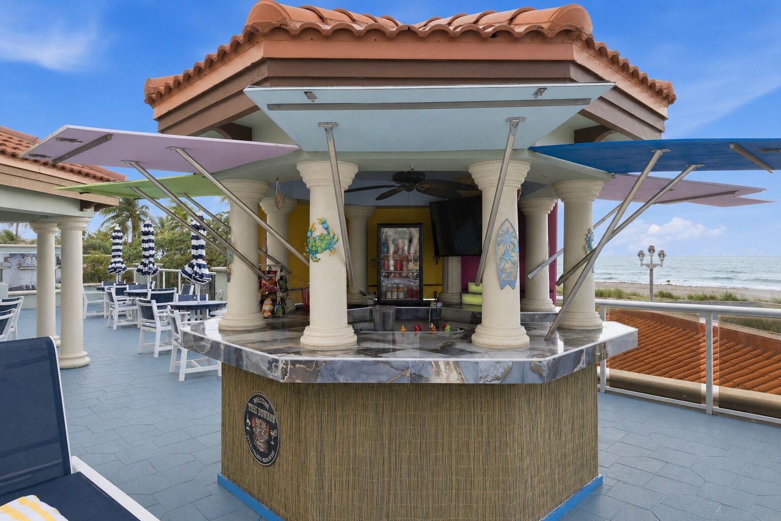 A bar area with a wooden counter, white pillars, and umbrellas.