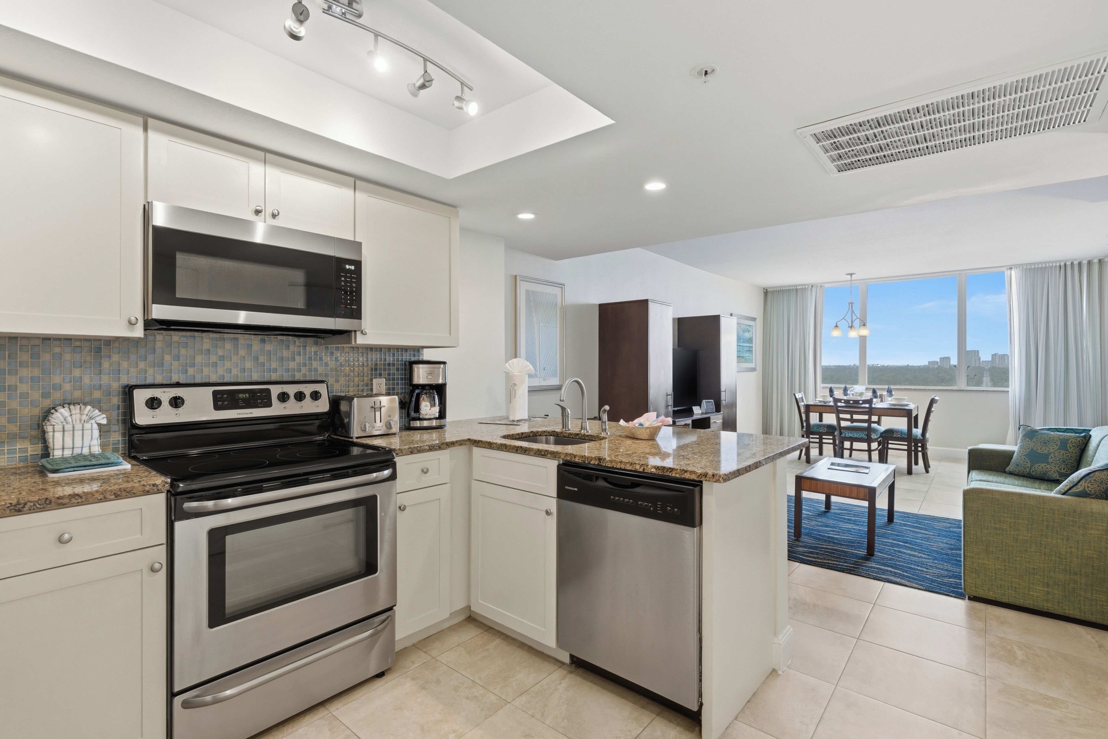 A modern kitchen with stainless steel appliances, a dining area with a view, and a living room with a sofa.