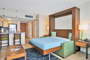 A hotel room with a large bed, a desk, two chairs, a nightstand, and a lamp. - Hollywood Beach Tower (Hollywood)