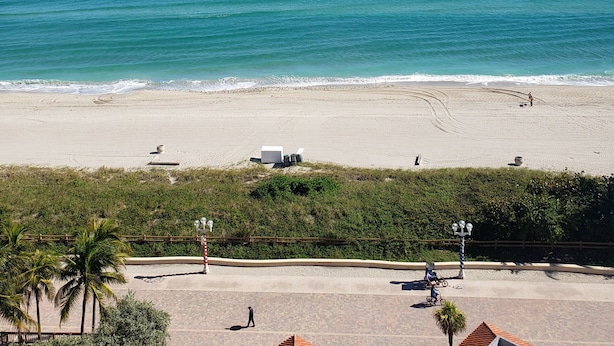 Een strand met een helder uitzicht op de oceaan, een zandstrand en enkele mensen die wandelen.