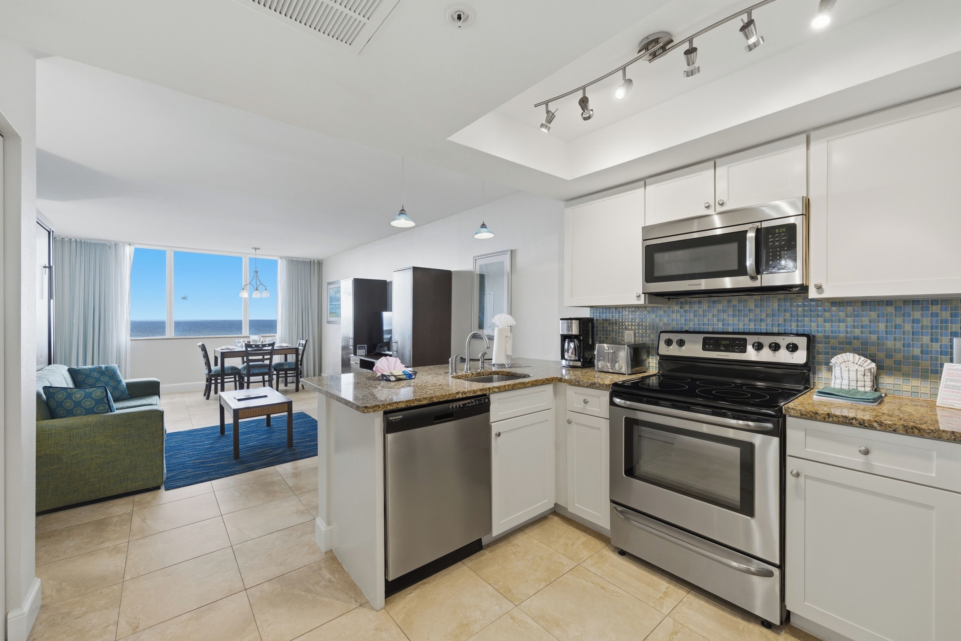 A modern kitchen with stainless steel appliances, a dining area with a view, and a living space with a sofa and a view.